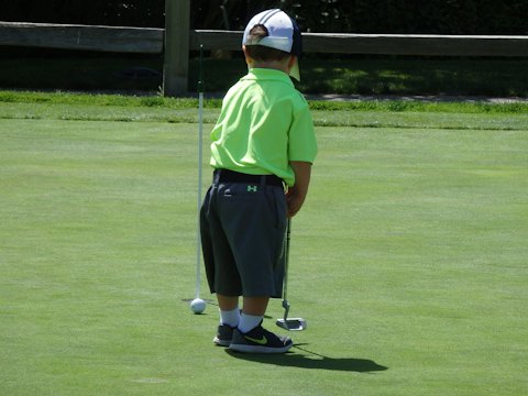 A young boy in a green polo shirt lining up a putt on a practice green